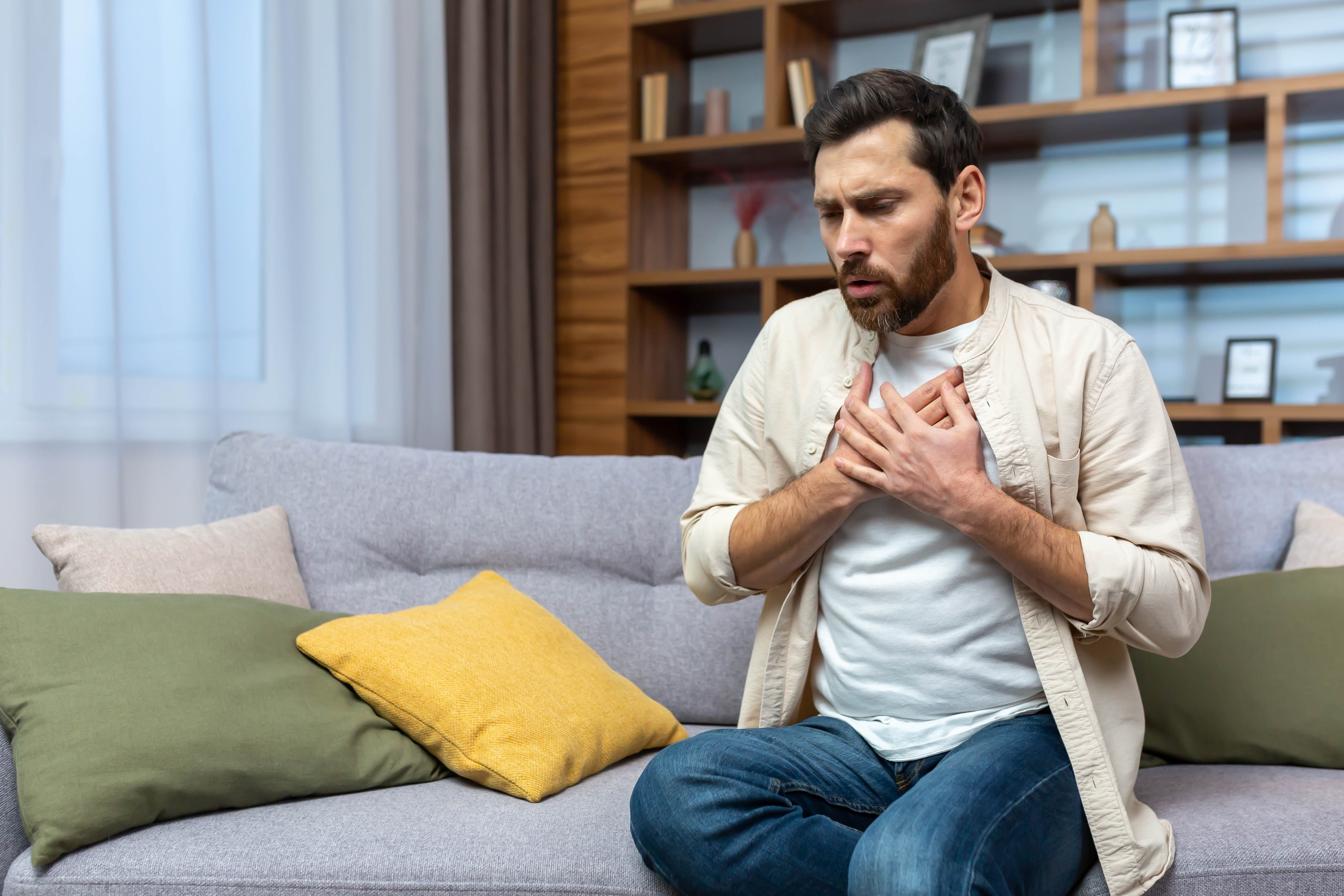 Man sitting on a couch, holding his chest, suffering from an anxiety and panic attack